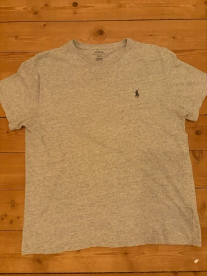  Polo Ralph Lauren T-shirt - Klassisk grå t-shirt från Polo Ralph Lauren med rund halsringning och den ikoniska broderade loggan på bröstet. Storlek M.