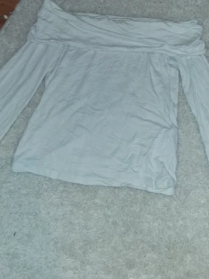 Vit offshoulder topp med lång ärm - Säljer en enkel och stilren vit offshoulder topp med långa ärmar. Toppen har en bred kant upptill som ger en snygg axelbar look. Perfekt att matcha med jeans eller kjol för en trendig outfit.