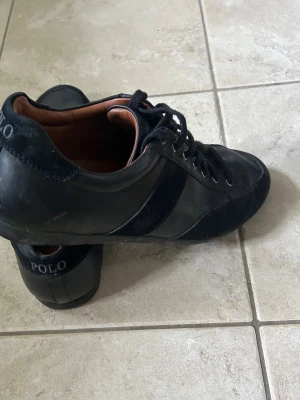 Svarta sneakers från Polo Ralph Lauren - Stilrena svarta sneakers från Polo Ralph Lauren med snörning och detaljer i skinn och mocka. Klassisk design med diskret logga på hälen och insidan. Perfekta för en clean och tidlös look.