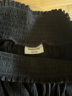 Svart volangkjol från Kappahl - Snygg svart kjol från Kappahl med bred smock i midjan och dubbla volanger. Kjolen är kort och har en luftig, flowy känsla som passar perfekt till många olika outfits.