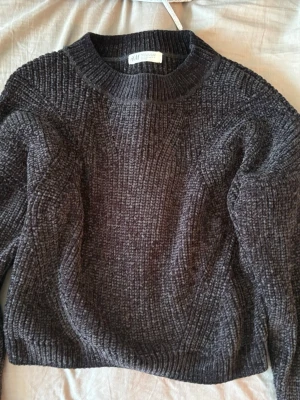 Svart chenilletröja från H&M - Mysig svart stickad tröja från H&M i mjukt chenillematerial. Tröjan har rund halsringning, ribbade muddar och en avslappnad passform. Perfekt för kalla dagar och enkel att matcha med jeans eller kjol.