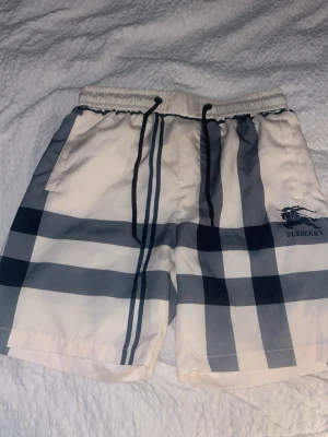BB shorts  - Säljer ett par snygga BB shorts med klassiskt rutigt mönster i vitt, grått och svart. Shortsen har elastisk midja med svart snörning och sidofickor. Perfekta för sommaren och har en avslappnad passform.