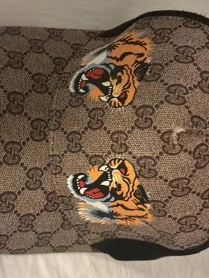 Brun keps med GG-mönster - Snygg brun keps med klassiskt GG-mönster .Kepsen har böjd skärm och svart mesh på sidorna. Perfekt för dig som vill sticka ut med en unik accessoar.
