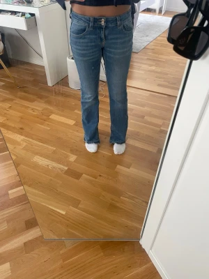 Blå bootcut jeans med hög midja - Säljer ett par klassiska blå bootcut jeans med hög midja och dubbla knappar i linningen. Jeansen har fyra fickor och är tillverkade i ett mjukt denimtyg med lätt stretch. Perfekta för en avslappnad och trendig look.