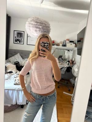 Ljusrosa stickad topp med kort ärm - Söt ljusrosa stickad topp med korta ärmar och ett luftigt hålmönster. Modellen är croppad och har ribbade muddar vid ärmslut och nederkant. Perfekt för en trendig och avslappnad look.