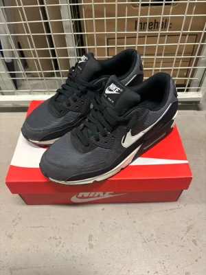 Nike Air Max 90  - Nike Air Max 90 – Black/White – Stl 44,5  Säljer ett par klassiska Nike Air Max 90 i svart/grått med vita detaljer.  Storlek: EU 44,5 Modell: Nike Air Max 90 Färg: Svart/grå/vit Skick: Begagnade i bra skick. Normalt bruksslitage och mindre märken förekommer, framför allt på mellansula och undersula. Se bilder för aktuellt skick. Tillbehör: Original Nike-skokartong medföljer.  Klassisk och lättmatchad Air Max-modell med synlig Air-dämpning.