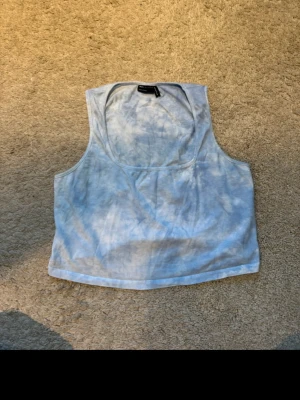 Blåvit croppad linnetopp - Säljer en croppad linnetopp i blått och vitt med tie-dye känsla. Toppen är ärmlös och har en rundad halsringning. Perfekt för sommardagar och enkel att matcha med jeans eller kjol.