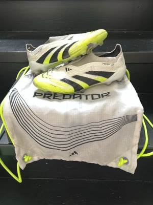 Adidas Predator fotbollsskor vit/gul - Säljer ett par Adidas Predator elite fotbollsskor laceless i vitt med svarta och neongula detaljer. Skorna har en strömlinjeformad design, låg vikt och mönstrad sula för bra grepp på planen. Ovandelen är i syntetmaterial och levereras med en matchande påse.