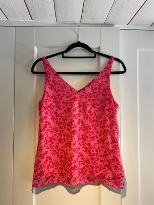 Rosa blommig linnetopp - Säljer en söt rosa linnetopp med små blommor i en mörkare rosa nyans. Toppen har v-ringning både fram och bak samt smala axelband. Perfekt för varma dagar och enkel att styla med jeans eller kjol.