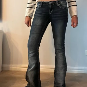 Mörkblå bootcut jeans med kontrastsömmar - Snygga mörkblå bootcut jeans med slitningar och vita kontrastsömmar. Jeansen har fem fickor och markerade sömmar på bakfickorna. Tillverkade i stretchigt denim för skön passform och en trendig look. Jag klippte bort fickorna för att göra det extra snygga!💗 Det är mörk blå/svart med urtvättning!