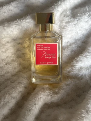 Eau de Parfum - Elegant parfymflaska med guldigt lock och genomskinligt glas. Innehållet är ljusgult och etiketten är röd med vit text. Flaskan har en stilren, fyrkantig form och rymmer 100 ml Eau de Parfum. Perfekt för dig som gillar lyxiga dofter.