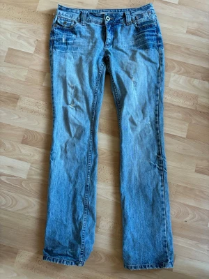 Ljusblå jeans - Säljer ett par ljusblå jeans med slitningar och tvättade detaljer. Jeansen har klassisk femficksmodell, normal midja och bootcut passform. Materialet är denim i bomull. Perfekta för en retro och  trendig look.