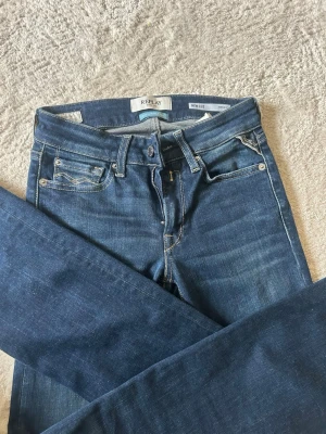 Blå raka jeans från Replay - Snygga blå jeans från Replay med raka ben och klassisk femficksmodell. Jeansen har kontrastsömmar och en liten logga på bakfickan. Tillverkade i ett mjukt denimtyg som sitter skönt. Perfekta till vardagslooken!