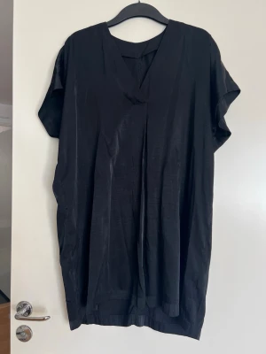 Svart tubika - Glansig tunika i svart! Hyfsat skick, har blivit lite noppor här och var. Inköpt på H&M storlek Small.   Längd: ca 83 cm fram / 92 cm bak
