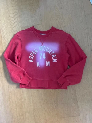 Jättefin populär Zara tröja! - Cool populär röd sweatshirt med trycket 'Aspen Mountain 74 AM' i vitt framtill. Endast använd 1 gång! Tröjan är perfekt nu inför hösten och slutet på sommaren! Färgglad men cool!  Tröjan har rund halsringning, ribbade muddar vid ärmar och nederkant samt en avslappnad passform. Materialet känns mjukt och bekvämt, perfekt för en avslappnad stil. Axelbredd: 45cm, längd: 48cm. Är en ganska kort modell så passar både S och xs! Skriv om frågor!