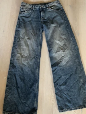 Blåa wide leg jeans med slitningar - Säljer ett par blåa jeans med breda ben och slitna detaljer. Jeansen har klassisk femficksmodell, hög midja och en tvättad look som ger en cool vintagekänsla. Materialet är denim i bomull och passformen är relaxed och loose fit.