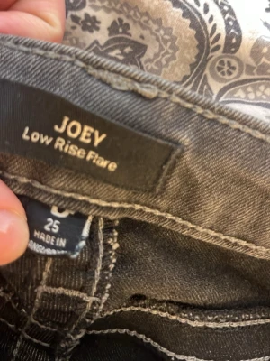 Mörkgrå true religion jeans - Säljer ett par mörkgrå bootcut jeans med snygga fickdetaljer och knappar bak. Jeansen har låg midja och klassisk femficksmodell. Materialet är stretchigt denim som sitter tajt upptill och släpper ut vid bensluten. Superfina men lite slitet vid fötterna. Ser värre ut än det faktiskt är! W25, sitter som xs/s