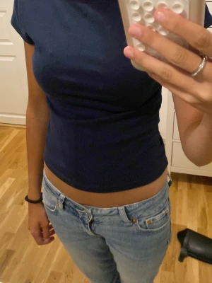 Mörkblå croppad t-shirt - En enkel och stilren mörkblå croppad t-shirt med korta ärmar och rund hals. Toppen har en tight passform och öppen rygg som ger en snygg detalj. Perfekt att matcha med jeans eller kjol för en trendig look.
