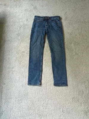Blå raka jeans med klassisk passform - Säljer ett par blå jeans med rak passform och normal midja. Jeansen har fem fickor och subtila slitningar framtill för en avslappnad look. Tillverkade i klassisk denim med lätt tvättad effekt. Perfekta till vardagsstilen.Jeans till salu Snygga blå jeans i fint skick. Klassisk modell med rak/slimmad passform. Jeans till salu Snygga blå jeans i fint skick. Klassisk modell med rak/slimmad passform. 