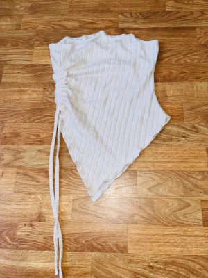 Beige ribbad omlottopp med snörning - Beige ribbad topp med asymmetrisk skärning och snörning i sidan. Toppen är ärmlös och har en omlott-look.