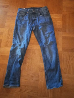 Blå raka jeans i klassisk modell - Säljer ett par blå jeans med rak passform och fem fickor. Jeansen har en klassisk midja och är tillverkade i denim med lätt tvättad look. Perfekta för dig som gillar en enkel och tidlös stil.