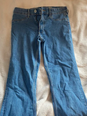 Blå bootcut jeans med fickor  - Säljer ett par klassiska blå bootcut jeans i denim med två bakfickor och bälteshällor. Jeansen har normal midja och raka ben som blir vidare nedtill. Perfekta för dig som gillar en retro och avslappnad stil.