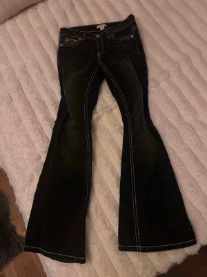 Svarta jeans med vita sömmar - Säljer ett par svarta bootcut jeans med markerade vita sömmar och broderade bakfickor💕 Jeansen har låg midja och klassisk femficksdesign. Jag är öppen för frågor och prisförslag💕