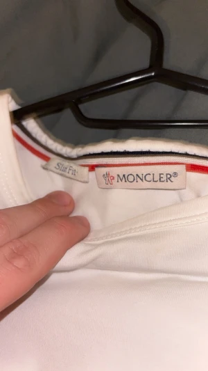 Vit slim fit t-shirt från Moncler - Säljer en vit slim fit t-shirt från Moncler med klassisk Moncler-logga på ärmen. T-shirten har korta ärmar och detaljer i rött och blått vid krage och ärmslut. Perfekt för dig som gillar stilrena och exklusiva plagg.