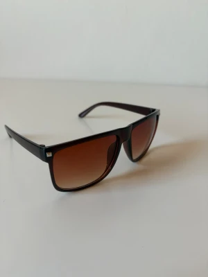 Svarta solglasögon med bruna glas - Snygga solglasögon med svart båge och fyrkantig form. Glasen är bruna med en snygg toning som ger en cool look. Perfekta för soliga dagar och ger en modern vibe till din outfit.