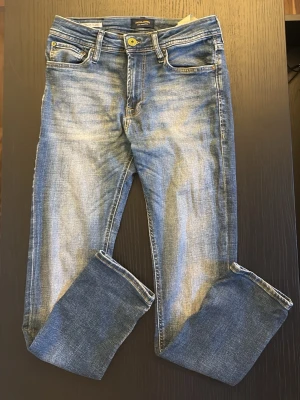 Ljusblå slitna jeans  - Säljer ett par ljusblå jeans från Jack & Jones med  modellen Regular Clark. De har storleken 28/30 och har även en Klassisk femficksmodell med gylf och knapp, samt läderpatch bak i midjan. Perfekta för en avslappnad och trendig look. 