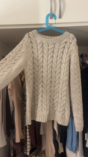 Beige kabelstickad tröja från H&M - Säljer en beige kabelstickad tröja från H&M i storlek M. Tröjan har ett klassiskt flätmönster, rund halsringning och ribbade muddar vid ärmslut och nederkant. Perfekt för kyliga dagar och enkel att matcha med olika outfits.