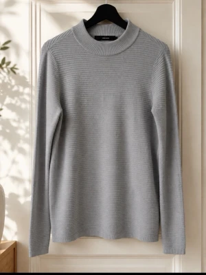 Ljusgrå stickad tröja Vero Moda - Snygg ljusgrå stickad tröja från Vero Moda med rund halsringning och långa ärmar. Tröjan har en enkel, stilren design med ribbstickade detaljer vid halsen. Perfekt att matcha med jeans eller kjol för en clean look.