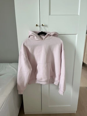 Ljusrosa oversized hoodie - En ljusrosa hoodie med oversized passform och stor känguruficka framtill. Tröjan har huva och ribbade muddar vid ärmslut och nederkant. Perfekt för en chill och avslappnad stil. Materialet ser ut att vara mjukt och skönt, troligen bomullsblandning.