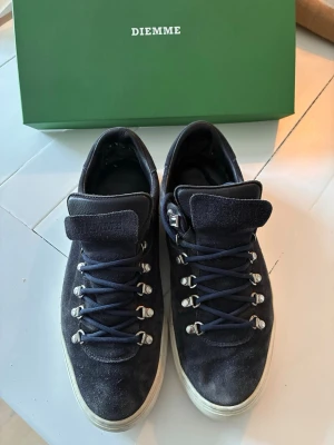 DIEMME Marostica Low Sneaker - Snygga mörkblå sneakers i mocka från Diemme med vita sulor och unika metallöglor för snörningen. Skorna har en låg profil och klassisk design som passar perfekt till streetwear och casual outfits. Påse och skokartong följer med.