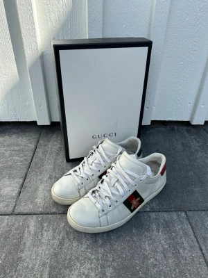 Gucci vita sneakers med bi-detalj - Snygga vita sneakers från Gucci med klassiska gröna och röda ränder på sidan samt en guldfärgad bi-detalj, nypris 8000kr|mitt pris 1799kr✅låda, snören mm följer med, dubbelboxar för frakt, hör av dig om du har fler frågor eller funderingar!