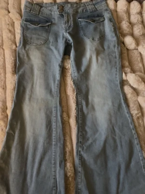 Ljusblå utsvängda jeans - Säljer ett par ljusblå jeans med utsvängda ben och stora fickor fram. Jeansen har knapp- och dragkedjestängning samt detaljerade sömmar. Perfekta för dig som gillar retrostil och vill ha ett par riktigt snygga jeans i garderoben.