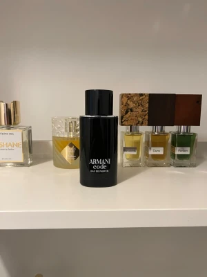 Armani Code Eau de Parfum - Armani Code Eau de Parfum från Giorgio Armani i en elegant svart flaska med matchande svart kartong. Doften är sofistikerad och modern, perfekt för dig som gillar exklusiva parfymer. Flaskan har en stilren, cylindrisk form och känns lyxig att hålla i handen.