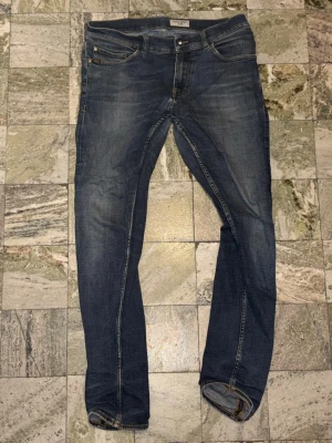 Tiger of Sweden Mörkblå slim fit jeans  - Säljer ett par mörkblå slim fit jeans med snygga slitningar och klassisk femficksdesign. Jeansen har smala ben och kontrastsömmar, samt en läderpatch bak i midjan. Gjordes av tiger of Sweden