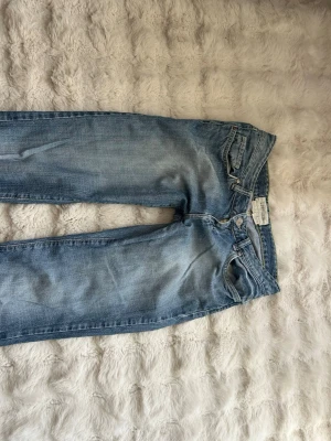Ljusblå raka jeans - Säljer ett par ljusblå jeans med rak passform och klassisk femficksdesign. Jeansen har dragkedjegylf och bälteshällor. Materialet är denim i bomull och de har en snygg tvättad look med subtila slitningar.