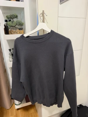 Mörkgrå stickad tröja från Zara - En enkel och stilren mörkgrå stickad tröja från Zara. Tröjan har rund halsringning med ribbad kant och långa ärmar. Materialet känns mjukt och passar perfekt till lager på lager. Snygg att matcha med jeans eller kjol.