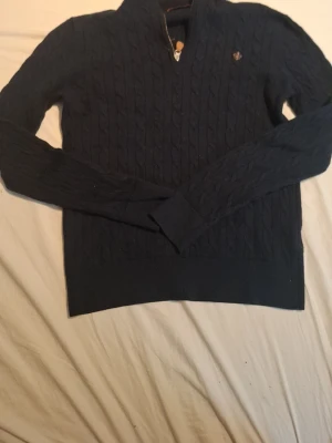 Mörkblå kabelstickad tröja halvzip - Mörkblå Morris tröja med halv dragkedja och broderad detalj på bröstet. Tröjan har långa ärmar och ribbade muddar. Perfekt för lager på lager och ger en klassisk look. Skriv gärna för frågor! Har krympt lite i tvätten så är kanske mer som en xs.