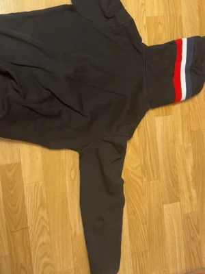 Moncler Svart hoodie med dragkedja  - Svart moncler  hoodie med hel dragkedja och huva. Huvan har breda ränder i rött, vitt och blått. Tröjan har fickor framtill och muddar vid ärmslut. 