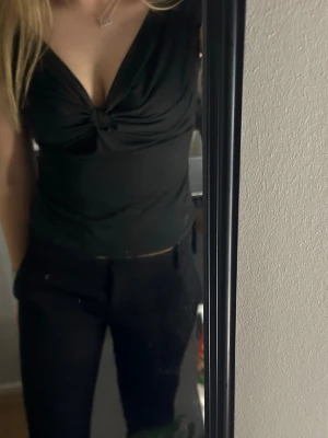 Svart croppad topp med v-ringning - Snygg svart croppad topp med djup v-ringning och twistad detalj framtill. Toppen är ärmlös och har en tight passform som framhäver figuren. Perfekt för dig som vill ha en stilren men ändå trendig look.