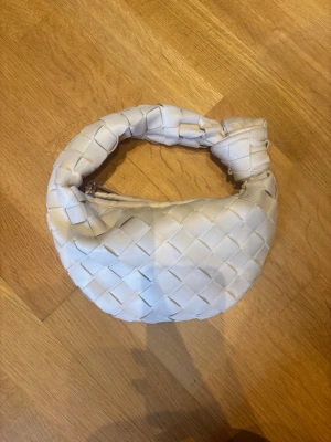 Flätad beige väska  - Söt beige flätad väska med en knut. Tyvärr har den gått sönder inuti och därmed säljer jag den. Den går att sy ihop, och bli fin igen!! Utifrån insidan är utsidan i bra skick utan fläckar. 🤗 köptes för 550kr. Men med tanke på defekt säljer jag den för 300kr.