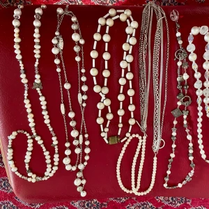 Mix av pärlhalsband och kedjor - Samling med flera halsband i olika stilar, bland annat klassiska pärlhalsband i vitt och beige, halsband med silverkedjor och detaljer som fjärilar, hjärtan och berlocker. Några har inslag av bruna pärlor och glittriga kristaller. Perfekt för dig som gillar att variera din look med unika smycken.