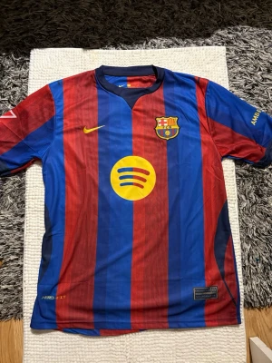 Barcelona matchtröja Nike röd/blå - Säljer en officiell FC Barcelona matchtröja från Nike med klassiska röda och blå vertikala ränder. Tröjan har klubbmärke, Nike-logga och Spotify som sponsor på bröstet. Tillverkad i lätt och ventilerande material, perfekt för fotboll eller träning. Köpt utomlands
