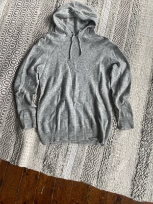 Grå Kashmir hoodie  - En riktigt snygg grå Kashmir hoodie. Med ribbade muddar vid ärmslut och nederkant. Perfekt för en avslappnad look och enkel att matcha med andra plagg. Det är dock hål på båda armdågarna de ser man på bilderna. Förutom det är tröjan i bra skick med lite noppror. Jag har växt ur tröjan därav får ingen användning av den längre de resulterar i det billiga priset.