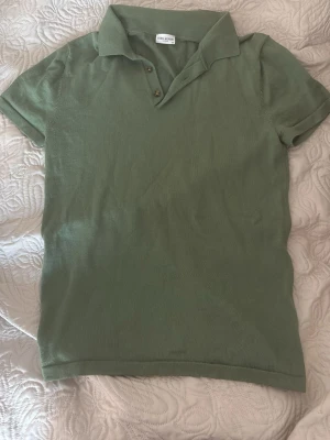 Grön piké från John Henric - Snygg grön pikétröja från John Henric med klassisk krage och två knappar framtill. Tröjan är kortärmad och har en stilren, enkel design som passar perfekt till jeans eller shorts. Tillverkad i mjukt material för skön känsla.