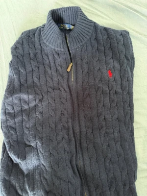 Två kabelstickade tröjor från Polo Ralph Lauren och en grå tröja - Säljer två kabelstickade tröjor från Polo Ralph Lauren. En är mörkgrå med dragkedja och röd logga, den andra är ljusgrå med rund hals och svart logga. Båda har klassisk kabelstickad design och ribbade muddar. Perfekta för lager på lager och snygg stil. Har även en grå tröja. Säljer då de inte passade, aldrig använd endast provade. 1500 för alla 3 eller 600 st.