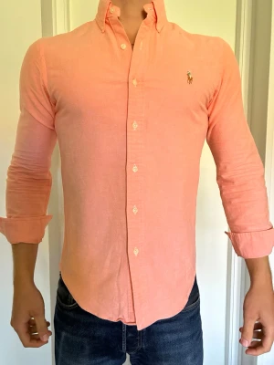 Orange skjorta från Ralph Lauren S - Snygg orange skjorta från Ralph Lauren i slim fit-modell. Skjortan har klassisk krage med knappar, lång ärm och broderad logga på bröstet. Tillverkad i stretchig bomull för extra komfort. 10/10 skick